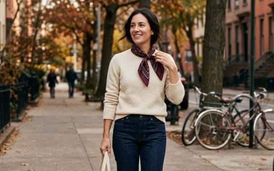 Woman wearing a patterned scarf with a cream sweater and dark jeans on a fall day.
